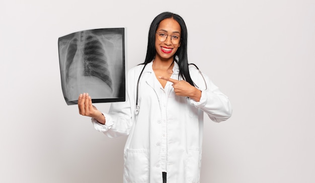 Young woman smiling cheerfully, feeling happy and pointing to the side and upwards, showing object in copy space