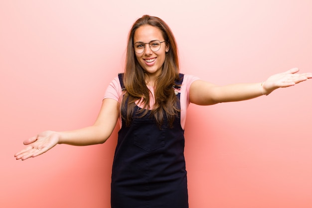 Young  woman smiling cheerfully giving a warm, friendly, loving welcome hug, feeling happy and adorable against pink wall