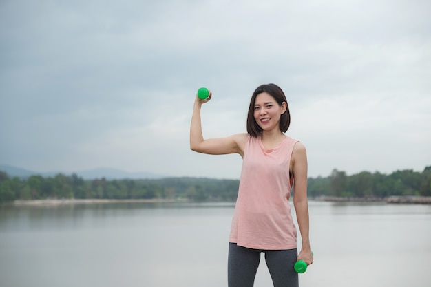 若い女性は公園でダンベル運動を笑っています。健康的なライフスタイルのコンセプト。