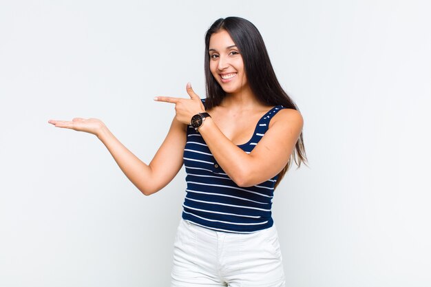 Young woman smiling, feeling happy, carefree and satisfied, pointing to concept or idea on copy space on the side