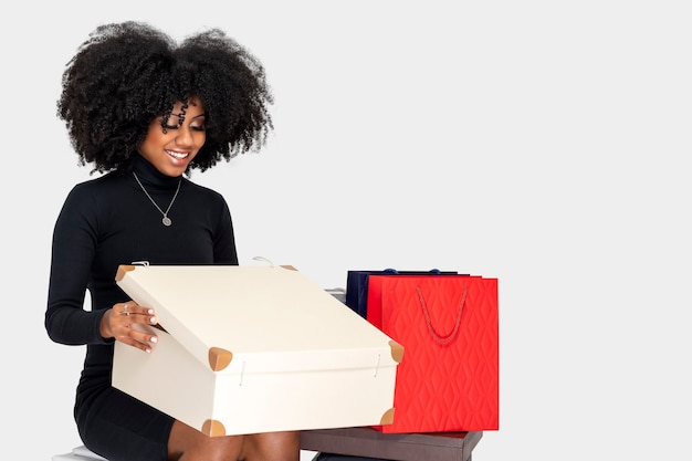 YOUNG WOMAN SMILING HAPPILY AS SHE OPENS GIFT BOX SITTING DOWN AND BESIDE HER SEVERAL SHOPPING BAGS