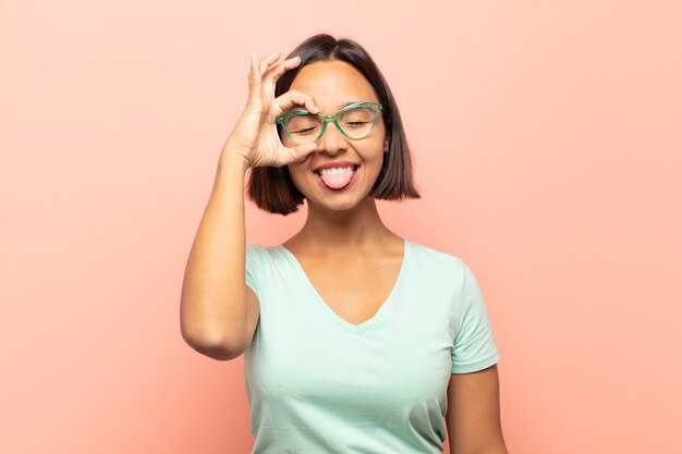 Young woman smiling happily with funny face, joking and looking through peephole, spying on secrets