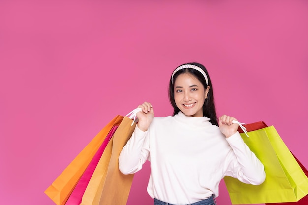 Young woman smiling and hold shopping bags and credit card while doing some shopping on a pink studio background