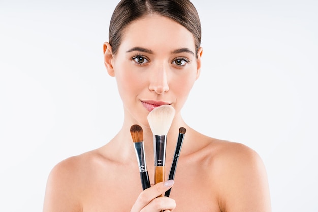 Young woman smiling and holding makeup brushes isolated on white background Cosmetic beauty concept