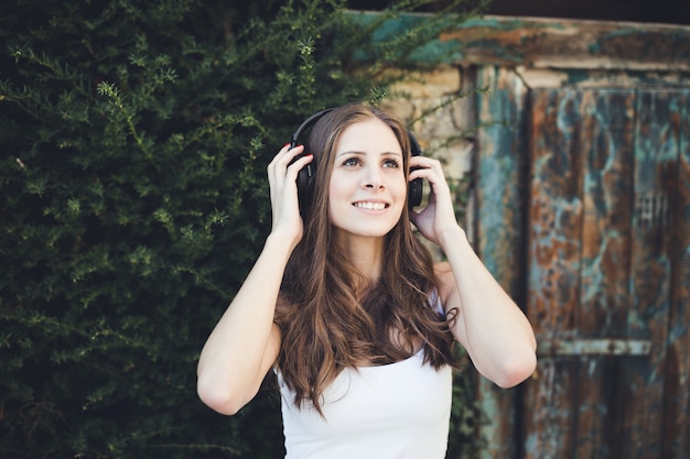 Young woman smiling and listening to music via headphones outdoors