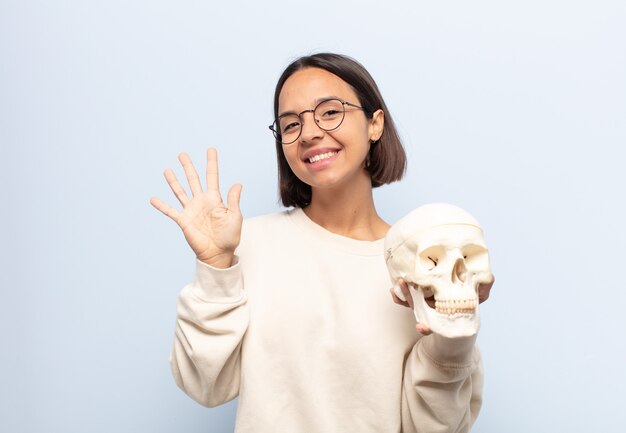 Giovane donna sorridente e dall'aspetto amichevole, mostrando il numero cinque o quinto con la mano in avanti