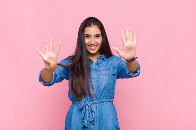 Giovane donna sorridente e guardando amichevole, mostrando il numero nove o nono con la mano in avanti, il conto alla rovescia