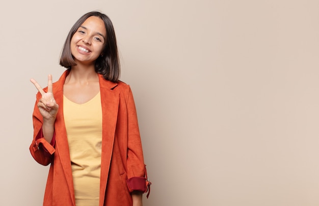 Young woman smiling and looking happy, carefree and positive, gesturing victory or peace with one hand