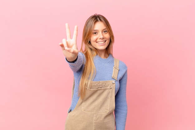 Young woman smiling and looking happy, gesturing victory or peace