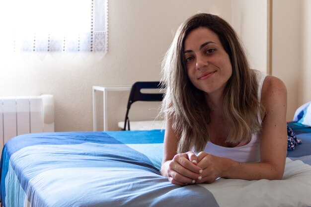 Young woman smiling lying on the bed in the room. Selective focus. Copy space.