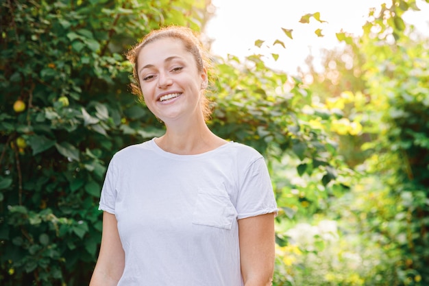 Giovane donna sorridente all'aperto bella ragazza bruna che riposa su sfondo verde parco o giardino donna felice libera in estate libertà felicità spensierata gente felice concetto