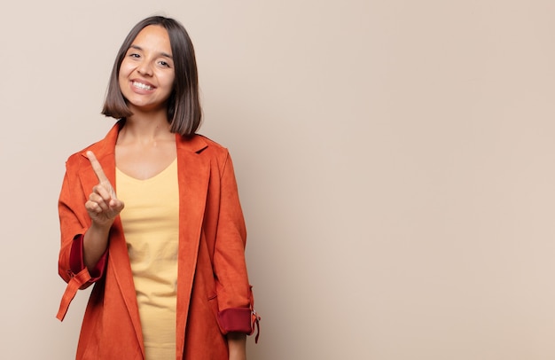 Young woman smiling proudly and confidently making number one pose triumphantly, feeling like a leader