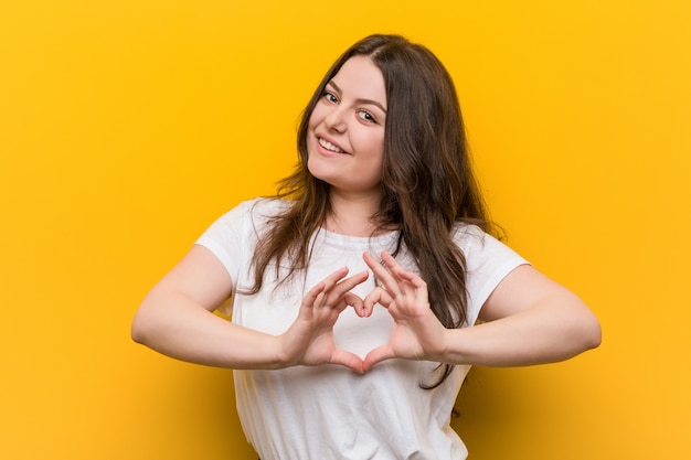 young woman smiling and showing a heart shape with him hands.
