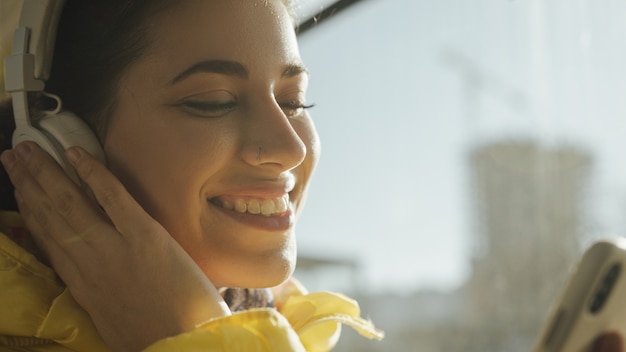 Young woman smiling while standing in train, tram or bus. Happy female passenger listening to music on a smartphone in public transportation.