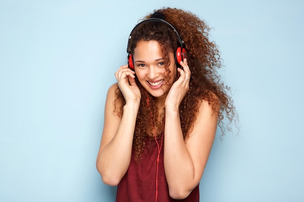 Young woman smiling with headphones by blue background