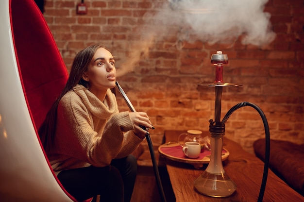 Young woman smokes hookah in bar, chill out