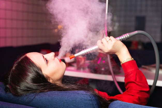 Young woman smokes a hookah or shisha in the club or bar smoke