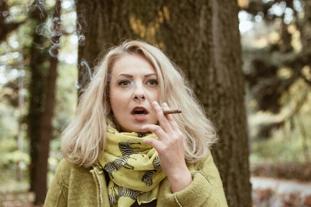 Young woman smoking cigar against tree trunk