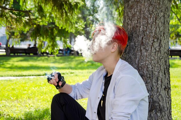 young woman smoking cigarette sits on lawn in the park