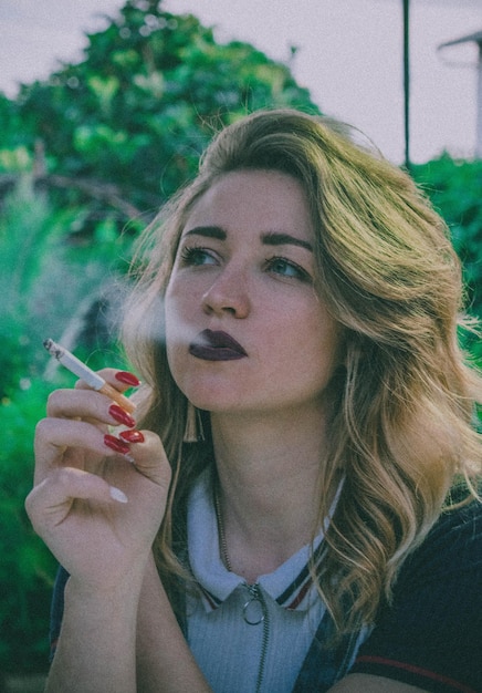 Photo young woman smoking cigarette while looking away against sky