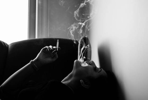 Photo young woman smoking cigarette while lying on sofa at home