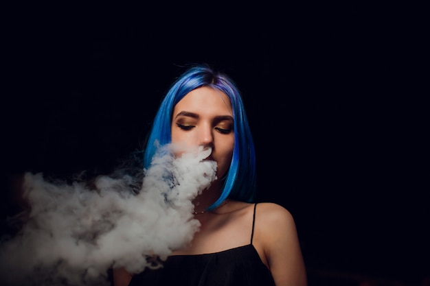 Photo young woman smoking electronic cigarette against a black background