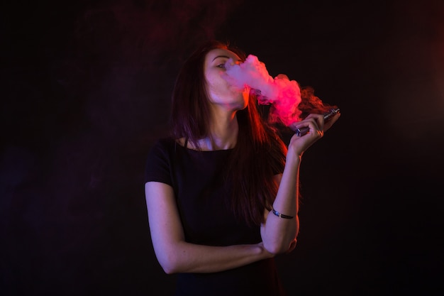 Young woman smoking electronic cigarette, cigarette smoke in light