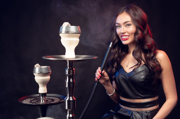 Photo young woman smoking a hookah on dark