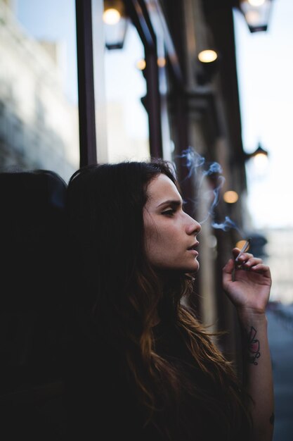 Foto giovane donna che fuma appoggiata alla finestra