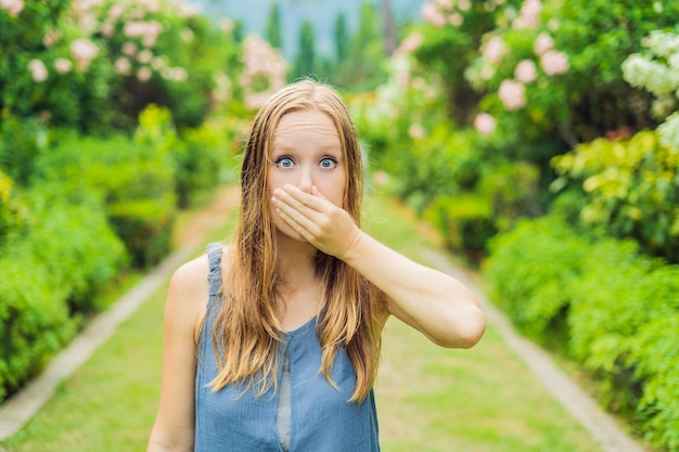 写真 花粉の概念に花の咲く木のアレルギーを背景に公園でくしゃみをする若い女性