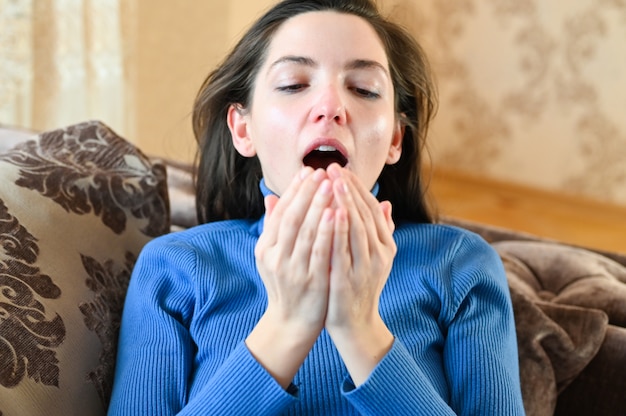 Young woman sneezes in the palm of her hand