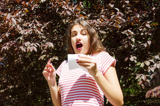 Young woman sneezing against plants during summer