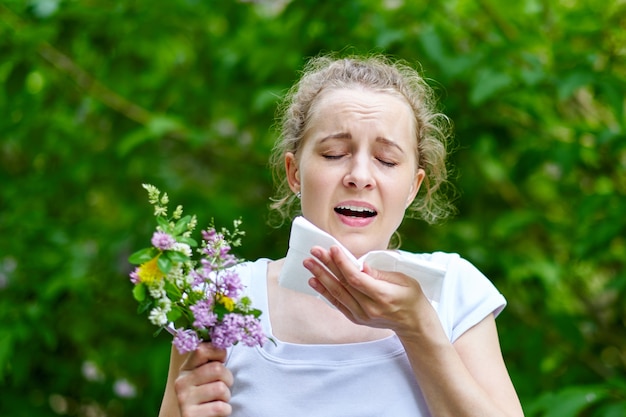 花の花束でくしゃみをする若い女性。概念：季節性アレルギー。