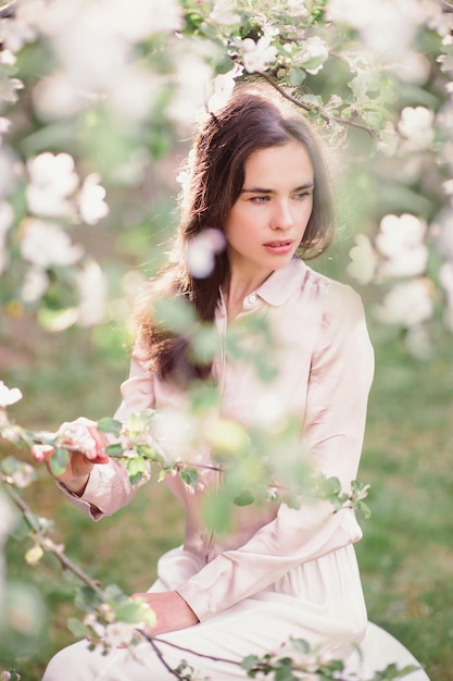 A young woman sniffs the aroma in a blooming apple garden in spring