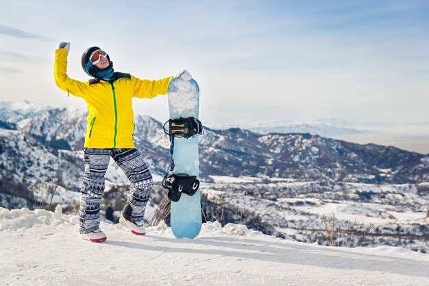 写真 雪山の背景に黄色のジャケットと黒のヘルメットの若い女性スノーボーダー。