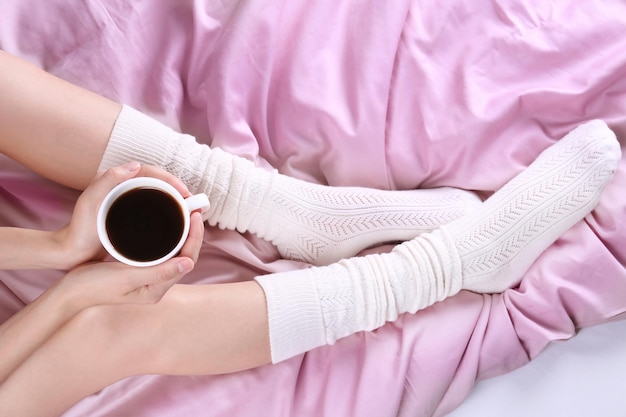 Young woman in socks with cup of coffee on bed