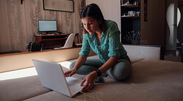 自宅のラップトップで新しいプロジェクトに喜んで取り組んでいるソファの上の若い女性