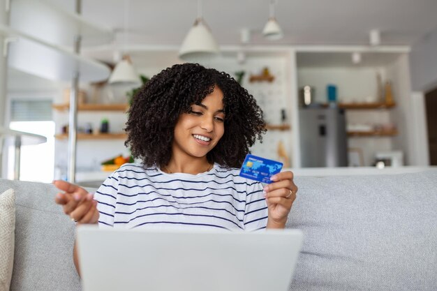 Giovane donna sul divano shopping online con carta di debito bella donna africana utilizzando il computer portatile per lo shopping online a casa