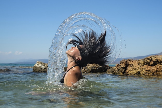 明るい空に照らして海に水を噴く若い女性