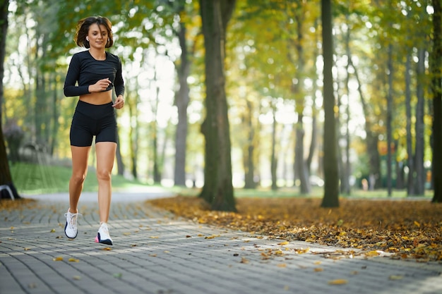 Молодая женщина в спортивной одежде и кроссовках на бегу в парке