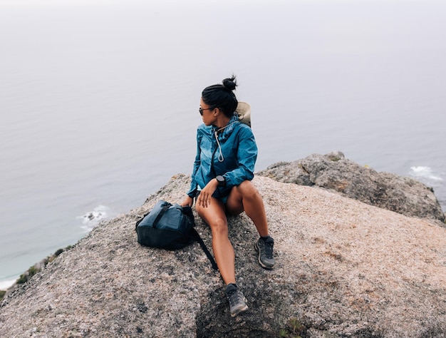 Young woman in sports clothes sitting on a big stone on a top of a mountain