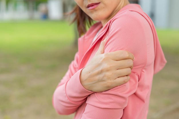 Giovane donna in abiti sportivi rosa si è ferita la parte superiore del braccio durante l'esercizio nel parco sezione superiore della ragazza sportiva che soffre di dolore al braccio mentre era seduto all'allenamento infortunio dal concetto di esercizio