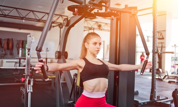 Young woman in sportswear doing exercise in exercise machine at the gym