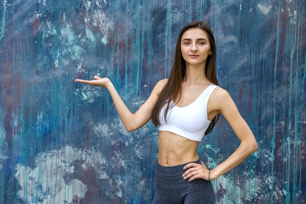 Young woman in sportswear gesturing on grey wall