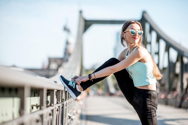 Молодая женщина в спортивной одежде делает утреннюю зарядку на железном мосту во Франкфурте