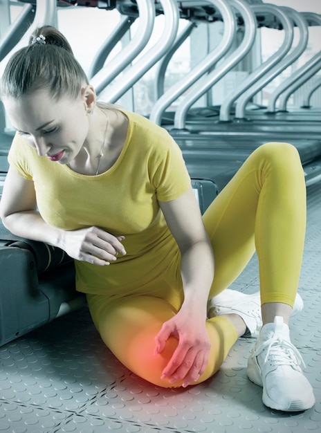 Foto giovane donna in abbigliamento sportivo che ha dolore al ginocchio durante l'allenamento in palestra ragazza seduta su un pavimento che tocca il ginocchio dolorante