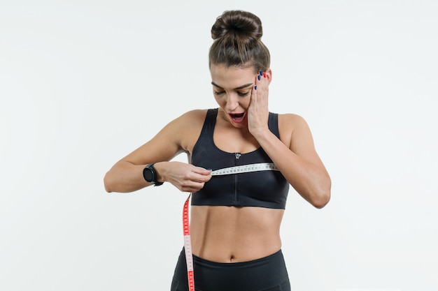 Young woman in sportswear is surprised holding a centimeter tape