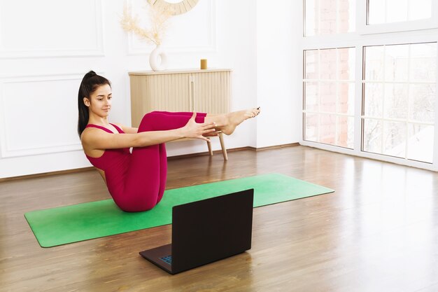 Young woman in sportswear practicing yoga exercising at home with an online trainer doing boat pose Paripurna Navasana