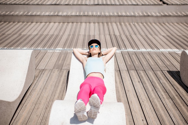 Young woman in sportswear resting after the training lying on the modern sunbed in the city