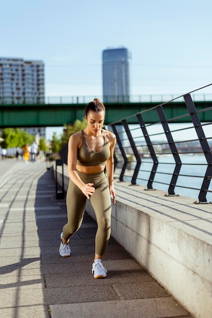 Giovane donna in abiti sportivi che si estende su una passeggiata sul fiume